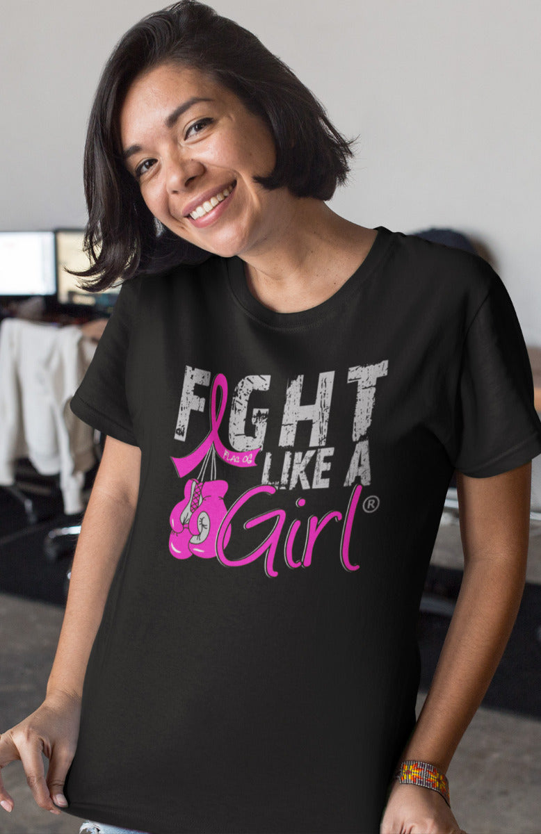 Woman wearing a black unisex t-shirt with the Fight Like a Girl Knockout design in pink on the front. The design says "Fight Like a Girl" and includes boxing gloves hanging from a pink awareness ribbon.
